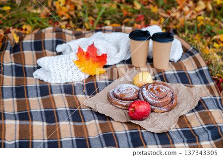 Cozy autumn picnic scene with plaid, knitted sweater, two paper cups of hot drinks, pastries, apples and falling maple leaves Cozy autumn picnic scene with plaid, knitted sweater, two paper cups of hot drinks, pastries, apples and falling maple leaves 137343305