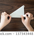 孩子的手在木桌上折一架銀色的摺紙飛機。 137343448