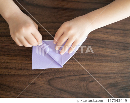 Child's hands folding purple origami paper on a wooden table 137343449