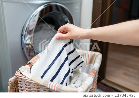 Woman's hand taking clothes from wicker basket to washing machine Woman's hand taking clothes from wicker basket to washing machine 137343453