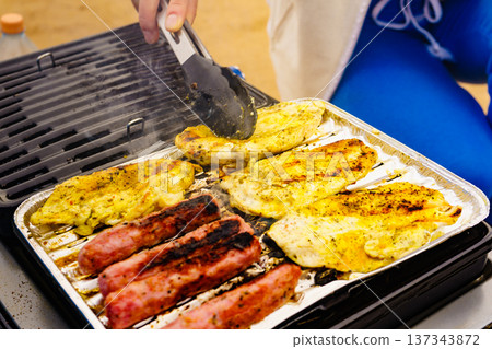 Hand grilling sausages and chicken meat on grill 137343872