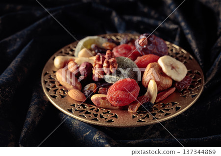 Dried tropical fruits and nuts in a golden bowl. Dried tropical fruits and nuts in a golden bowl. 137344869