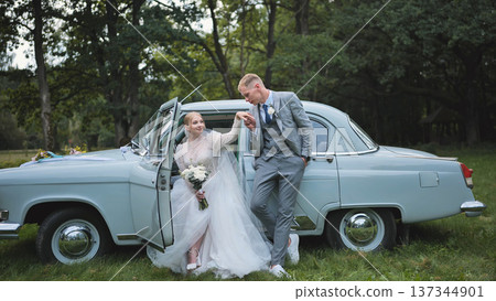 Elegant bride and groom celebrating their wedding day with a vintage car in a picturesque outdoor setting Elegant bride and groom celebrating their wedding day with a vintage car in a picturesque outdoor setting 137344901