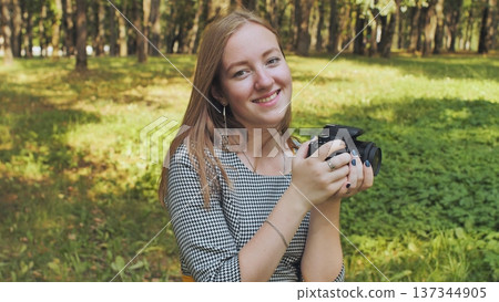 Young photographer smiling and holding a camera in a park, enjoying her passion for photography in nature Young photographer smiling and holding a camera in a park, enjoying her passion for photography in nature 137344905