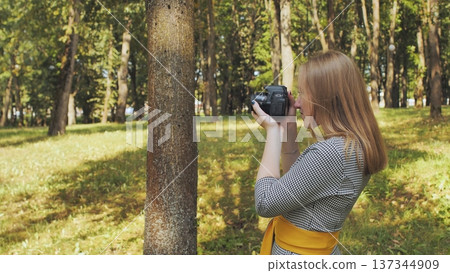 Young woman photographer taking pictures in a green park on a sunny summer day, using a professional camera Young woman photographer taking pictures in a green park on a sunny summer day, using a professional camera 137344909