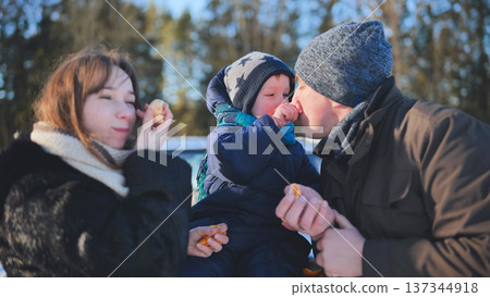 Happy family feeding tangerine segments to young child during bright winter afternoon outside 137344918