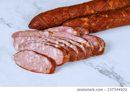 Sausage is sliced on marble surface with whole sausages placed behind cooking process in kitchen. 137344920