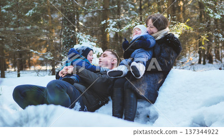 Family enjoying a joyful winter day, playing together in the snow amidst a beautiful forest filled with sunlight and frosty trees 137344922
