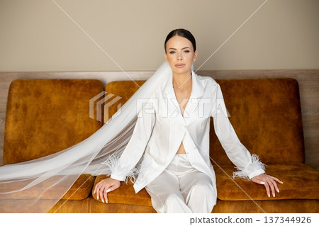 Bride relaxing on sofa wearing white pajamas and veil Bride relaxing on sofa wearing white pajamas and veil 137344926
