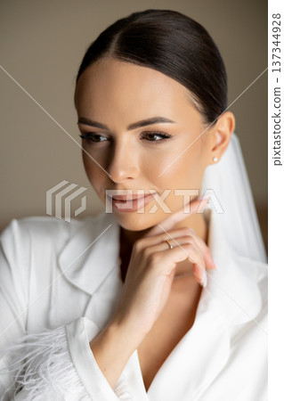 Beautiful bride wearing white silk pajamas, touching her chin and closing her eyes 137344928
