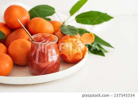 Glass jar of homemade marmalade with spoon and fresh tangerines on white table Glass jar of homemade marmalade with spoon and fresh tangerines on white table 137345334