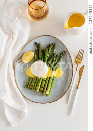 Grilled asparagus spears topped with poached egg and hollandaise sauce, garnished with fresh lemon wedge 137345353