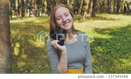 Young photographer smiling and holding a vintage camera in a park, enjoying her passion for photography and nature Young photographer smiling and holding a vintage camera in a park, enjoying her passion for photography and nature 137345448