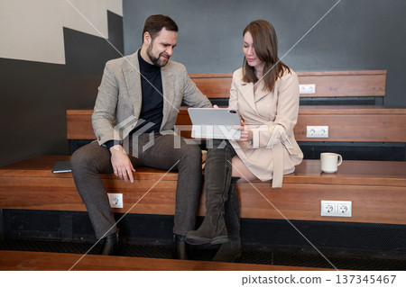 A man and woman using a tablet discuss information during a business meeting in stylish, minimalist office space. Technology businesses, startups, or coworking spaces, working with innovative tools. A man and woman using a tablet discuss information during a business meeting in stylish, minimalist office space. Technology businesses, startups, or coworking spaces, working with innovative tools. 137345467