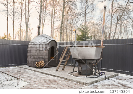 Calm hot water soak in wooden tub with sauna background during sunset Calm hot water soak in wooden tub with sauna background during sunset 137345804