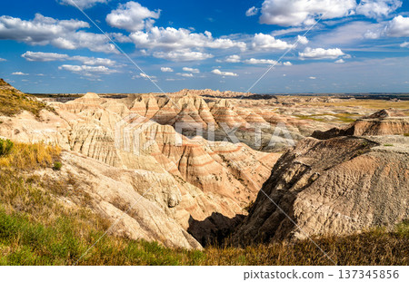 Scenic sunny view of the rugged layered rock formations and vast prairie landscape from Panorama Point in Badlands National Park, South Dakota, United States. Scenic sunny view of the rugged layered rock formations and vast prairie landscape from Panorama Point in Badlands National Park, South Dakota, United States. 137345856