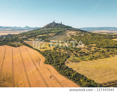 Hazmburk castle ruins rise majestically above the surrounding countryside in Czechia. This medieval structure offers panoramic views of the Central Bohemian Uplands and lush fields. Hazmburk castle ruins rise majestically above the surrounding countryside in Czechia. This medieval structure offers panoramic views of the Central Bohemian Uplands and lush fields. 137347045