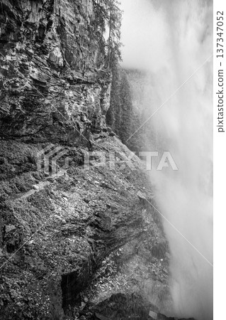 Johannes Waterfall cascades elegantly down rocky cliffs in Obertauern, Austria. Surrounded by alpine trees, the waterfall creates a misty atmosphere, perfect for nature lovers and hikers. 137347052