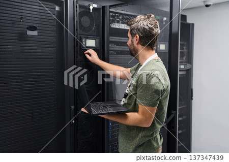 IT technician configuring server equipment in a data center while holding a laptop and checking network settings IT technician configuring server equipment in a data center while holding a laptop and checking network settings 137347439