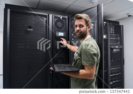 IT technician checking servers in a data center with laptop performing maintenance IT technician checking servers in a data center with laptop performing maintenance 137347441