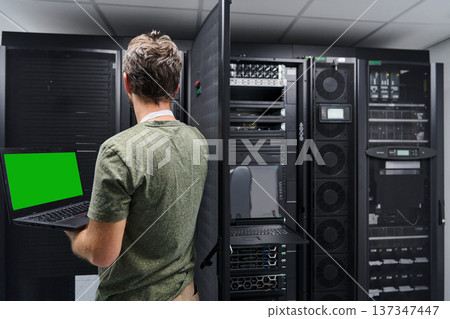 Data center technician using laptop to check server rack and network equipment in a server room Data center technician using laptop to check server rack and network equipment in a server room 137347447