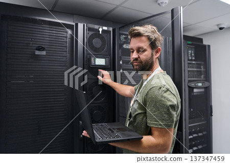 It technician working on servers in a data center with laptop checking rack equipment and controls It technician working on servers in a data center with laptop checking rack equipment and controls 137347459