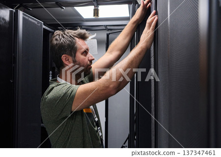 IT technician inspecting server rack in data center performing maintenance and hardware installation 137347461
