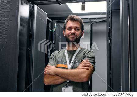 IT technician standing with arms crossed in a data center server room, confident and professional 137347465
