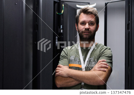 IT technician standing confidently in a data center server aisle with arms crossed IT technician standing confidently in a data center server aisle with arms crossed 137347476