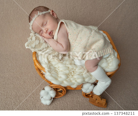 Full body portrait of a sleeping newborn baby girl in a wicker basket bed. Soft fabrics and neutral tones emphasize tenderness, parental care and the peaceful beauty of early infancy. Full body portrait of a sleeping newborn baby girl in a wicker basket bed. Soft fabrics and neutral tones emphasize tenderness, parental care and the peaceful beauty of early infancy. 137348211