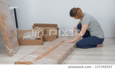 A Caucasian woman unpacks a box of furniture. A Caucasian woman unpacks a box of furniture. 137348507