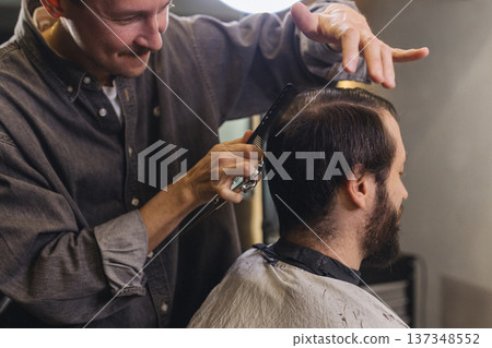 Barber cutting male client hair with scissors and comb. Close up of professional haircut process, precision technique, men grooming service in modern barbershop. 137348552