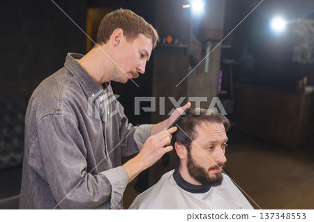 Barber cutting male client hair with scissors and comb. Close up of professional haircut process, precision technique, men grooming service in modern barbershop. Barber cutting male client hair with scissors and comb. Close up of professional haircut process, precision technique, men grooming service in modern barbershop. 137348553