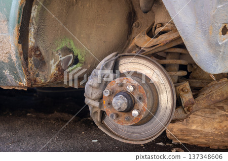 Car is missing one wheel in a garage with a clear view of the brake disc and pads, revealing the state of the vehicle in daylight Car is missing one wheel in a garage with a clear view of the brake disc and pads, revealing the state of the vehicle in daylight 137348606