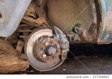 A car stands on the ground missing one wheel, revealing the brake disc. It is located by the roadside in daylight A car stands on the ground missing one wheel, revealing the brake disc. It is located by the roadside in daylight 137348607