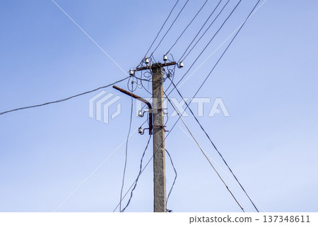 An electric pole supports multiple wires against a clear blue sky during daylight hours, showcasing utility infrastructure An electric pole supports multiple wires against a clear blue sky during daylight hours, showcasing utility infrastructure 137348611