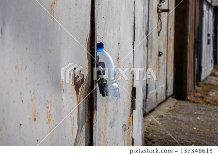 Garage doors are locked and secured. A bottle is placed in a keyhole, signaling that access is blocked or changed in this area 137348613