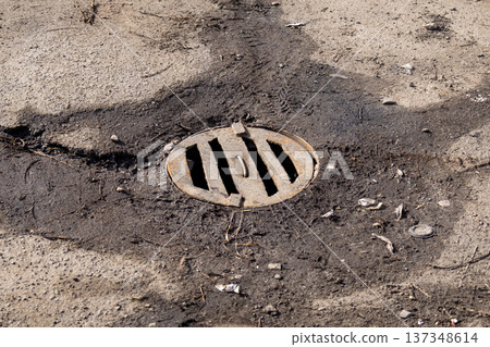 Manhole cover is placed on a concrete surface. Dirt and debris surround the cover under sunlight 137348614