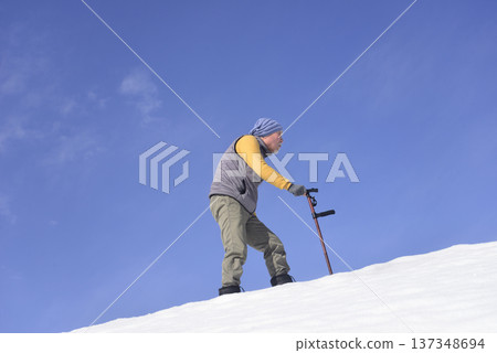 An elderly man living in a snowy rural area is using a walking stick for rehabilitation 137348694