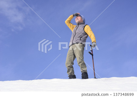 An elderly man living in a snowy rural area is using a walking stick for rehabilitation 137348699