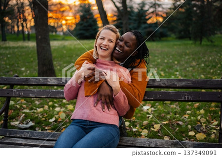 Happy diverse lesbian couple embracing in autumn park Happy diverse lesbian couple embracing in autumn park 137349091
