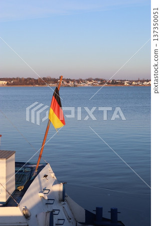 A German flag on the stern of a boat against the backdrop of a reservoir in the rays of the setting sun A German flag on the stern of a boat against the backdrop of a reservoir in the rays of the setting sun 137350051
