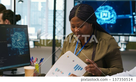 Joyous technician with disability and coworker chatting while coding AI algorithms debugging software issues. Upbeat tech startup office IT expert in wheelchair and colleague using computer, camera A 137350514