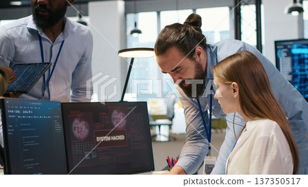 Young inexperienced developer in office requests help from team to fix hacking attempt on corporate network. Intern assisted by colleagues to investigate unauthorized access alerts, camera A 137350517