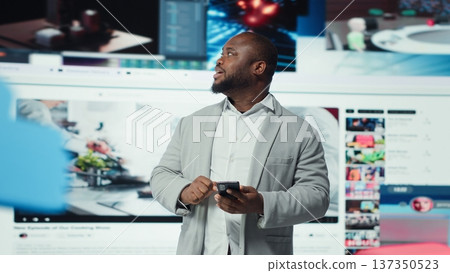 Happy person uses phone, interacting with social media posts on feed. Joyous man browsing social networks feed on smartphone in front of browser windows with short form content videos, camera A 137350523