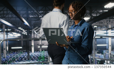 Data center engineer walking on industrial platform, running diagnostics on equipment to identify errors. Server farm IT professionals preventing rigs failure to minimize downtime Data center engineer walking on industrial platform, running diagnostics on equipment to identify errors. Server farm IT professionals preventing rigs failure to minimize downtime 137350544