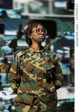 Soldier wearing camo uniform in command center, looking at multimedia display with tactical visuals. African american woman standing in front of defense headquarters videowall backdrop Soldier wearing camo uniform in command center, looking at multimedia display with tactical visuals. African american woman standing in front of defense headquarters videowall backdrop 137350557
