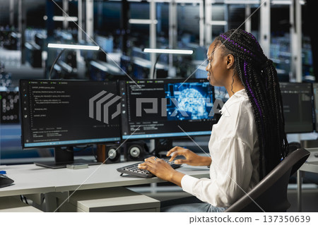Data center admin running simulations for neural network forecasting, tracking performance. African american woman in server hub integrating machine learning APIs into software platforms Data center admin running simulations for neural network forecasting, tracking performance. African american woman in server hub integrating machine learning APIs into software platforms 137350639