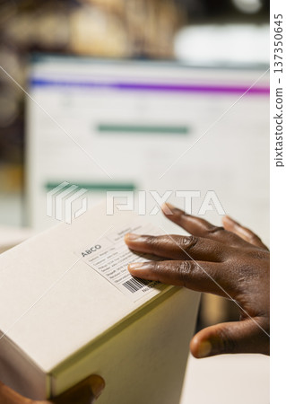 Close up of worker managing package labeling using shipment details adhesive tags, handling order processing and preparing the goods for delivery. Online shopping fulfillment center. 137350645