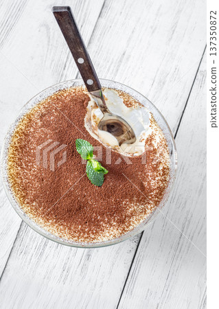 Close up tiramisu dessert in glass bowl with spoon revealing creamy layers Close up tiramisu dessert in glass bowl with spoon revealing creamy layers 137350872